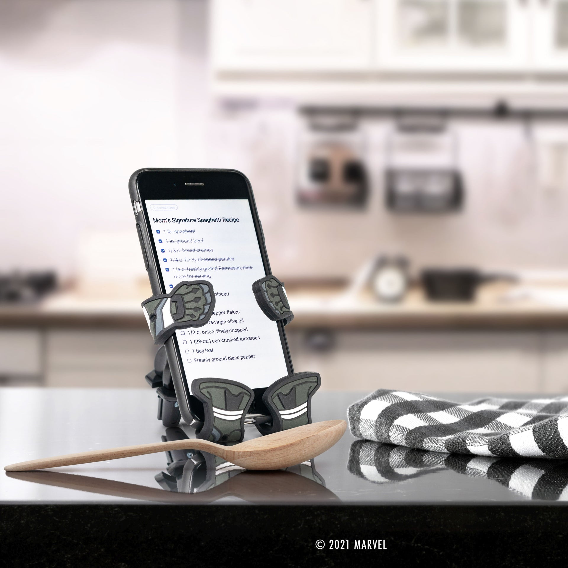 Image of Marvel Black Panther Hug Buddy holding a cell-phone while sitting on a kitchen counter, displaying a recipe on the phone screen.