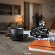 Image of Marvel Black Panther Hug Buddy holding a cell phone while sitting on a kitchen table next to a warm cup of coffee or tea
