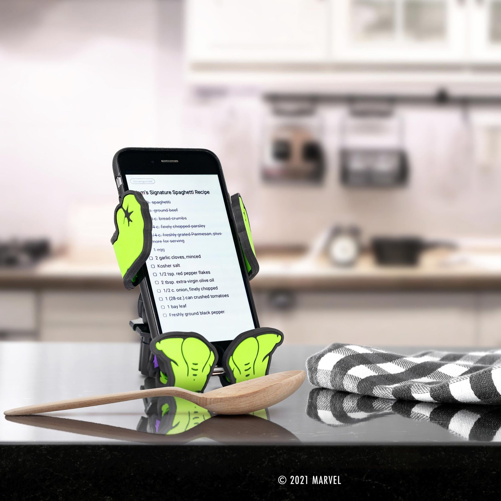 Image of Marvel Comics Hulk Hug Buddy holding a cell phone displaying a recipe while sitting on a kitchen counter by resting on its vent clip