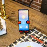 Image of Marvel Comics Iron Man Hug Buddy holding a cell phone while sitting on top of a kitchen dining table surrounded by dishware