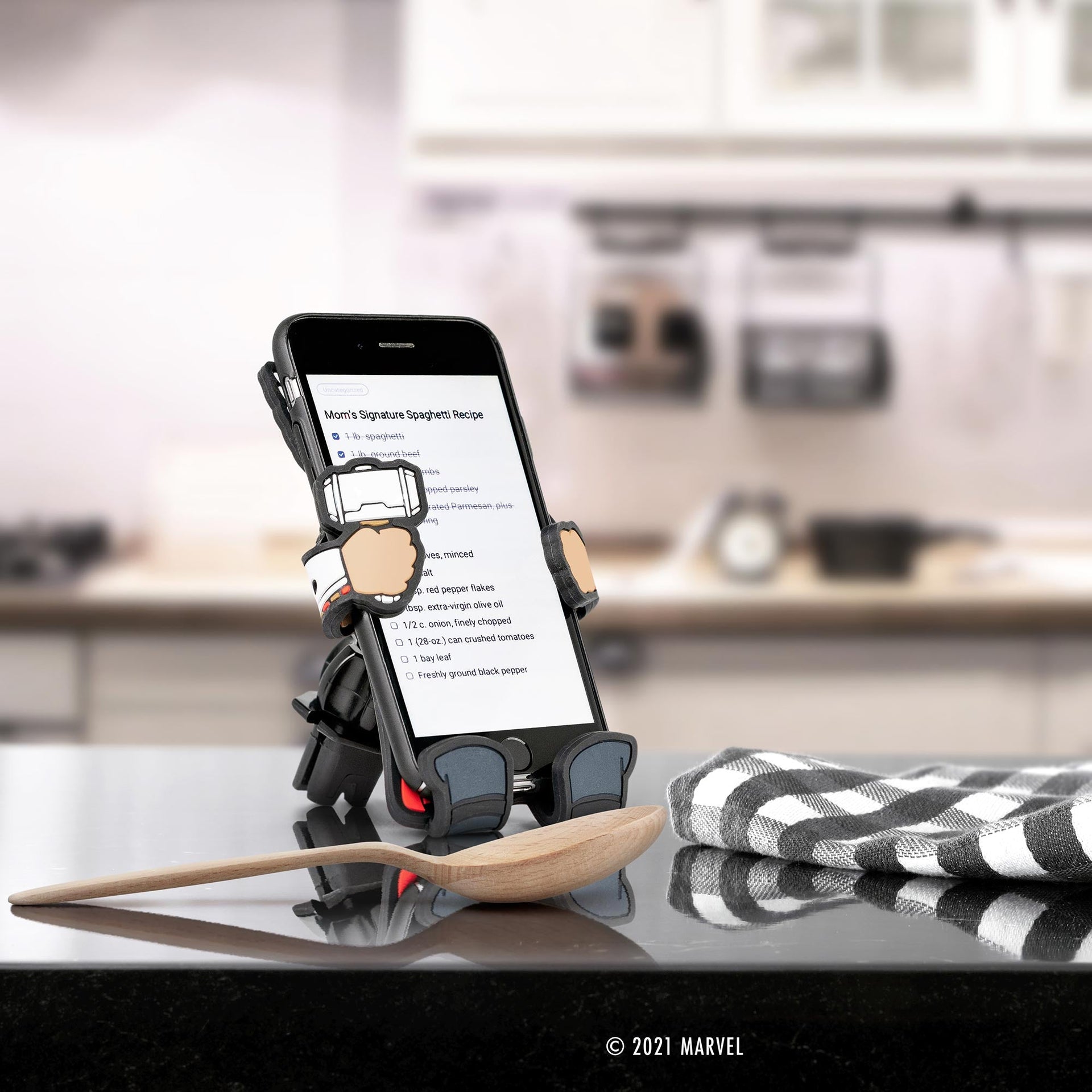 Image of Marvel Comics Thor Hug Buddy holding a phone with a recipe displayed on the screen, while resting on its vent clip on top of a kitchen counter