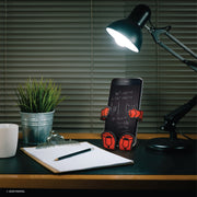 Image of Marvel Comics Iron Man Hug Buddy holding a cell phone while resting on its vent clip on top of a home office desk in the evening with a lamp shining down on the Buddy