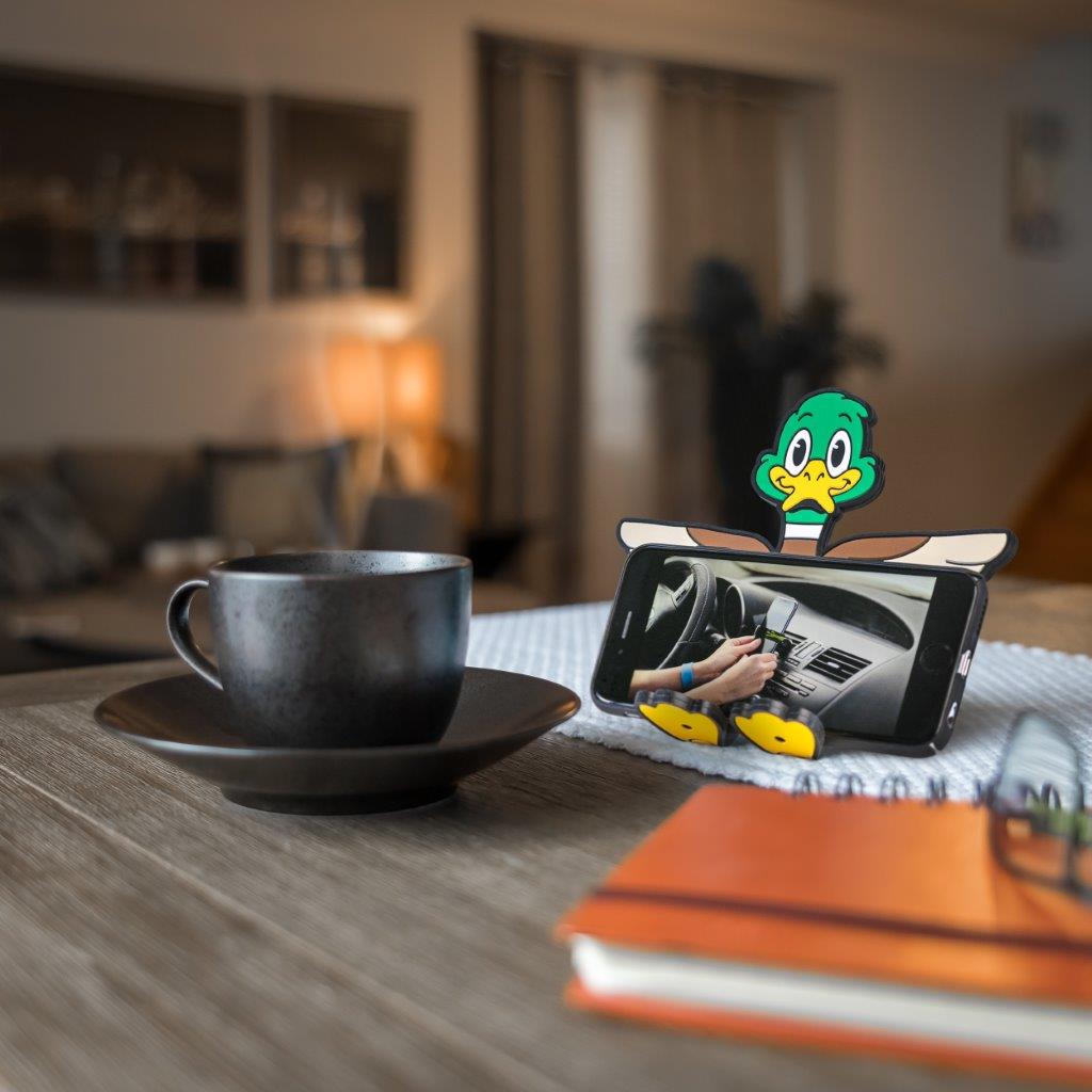 Image of Crumbs the duck Hug Buddy holding a phone while sitting on a kitchen island beside a warm mug of coffee or tea
