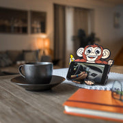 Image of Monkey Hug Buddy holding a cell-phone while sitting on a kitchen table with a warm cup of coffee or tea sitting beside it.