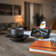 Image of Stripes the Eagle Hug Buddy holding a phone while sitting on a kitchen table next to a warm cup of coffee or tea