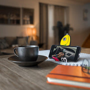 Image of Shaky the fish bait Hug Buddy on a kitchen table holding a phone beside a cup of coffee