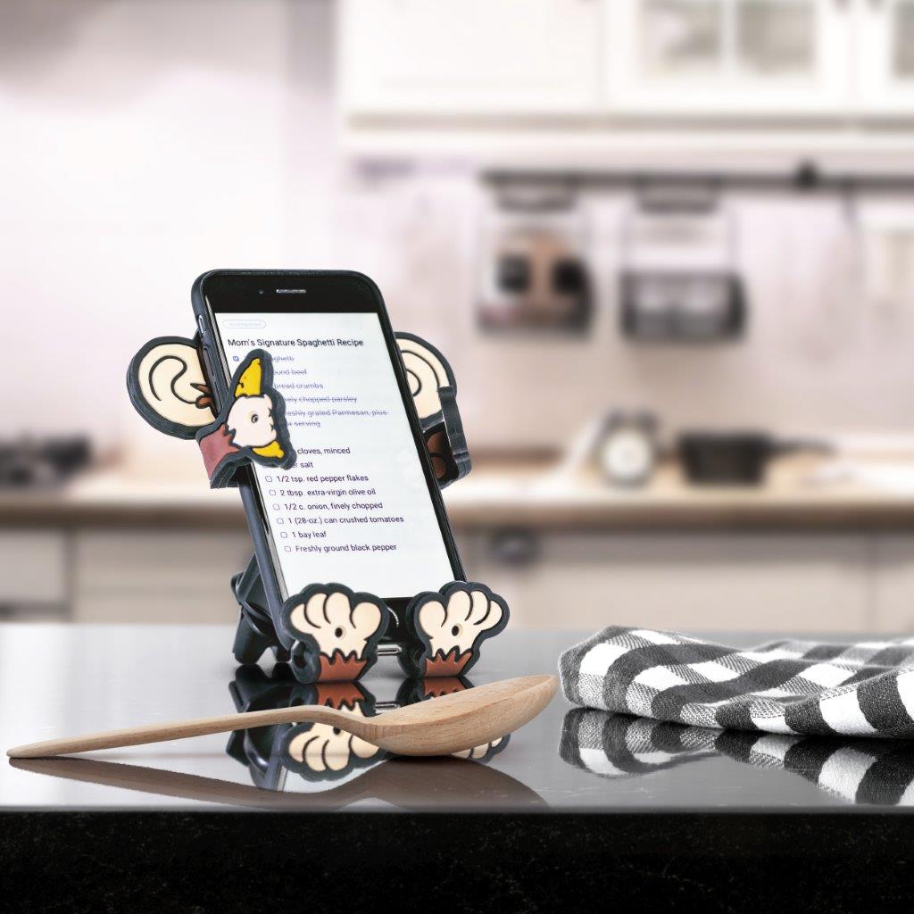 Image of Monkey Hug Buddy sitting on a kitchen counter holding a cell-phone with recipes on the screen.