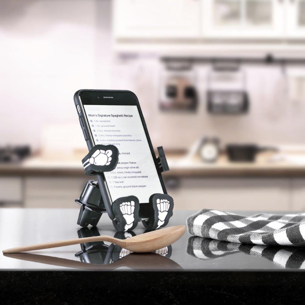 Image of Bones the Skeleton Hug Buddy holding a phone with a recipe displayed on screen, sitting on a kitchen counter