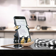 Image of Sloth Hug Buddy holding a cell phone with a recipe displayed on screen. The Hug Buddy is resting on its vent clip on top of a kitchen counter or island.