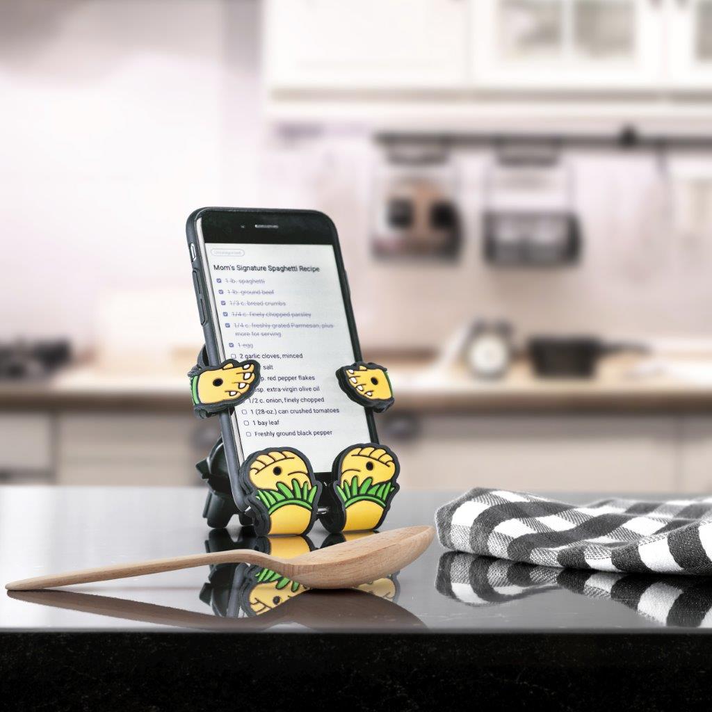 Image of Hula Girl Hug Buddy holding a cell-phone on top of a kitchen island or countertop, displaying a recipe on the phone screen