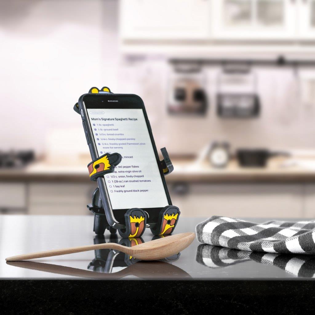 Image of Shorty the Giraffe Hug Buddy holding a cell phone while resting on top of a kitchen counter, displaying a recipe on the phone screen