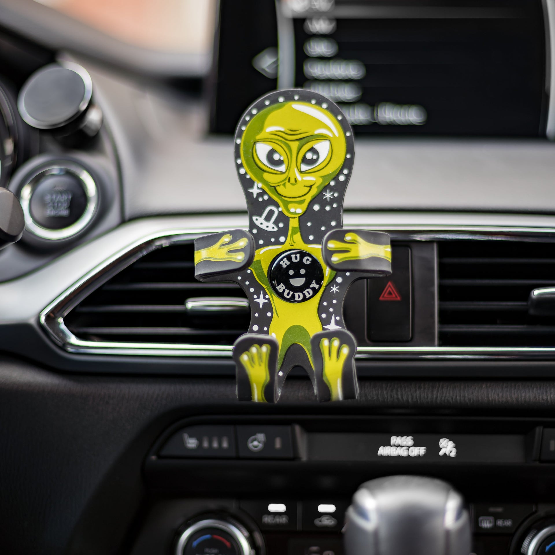 Image of Alien Hug Buddy attached to a vehicle air vent, arms and legs folded in, ready to hold your cell-phone or any device during your next drive