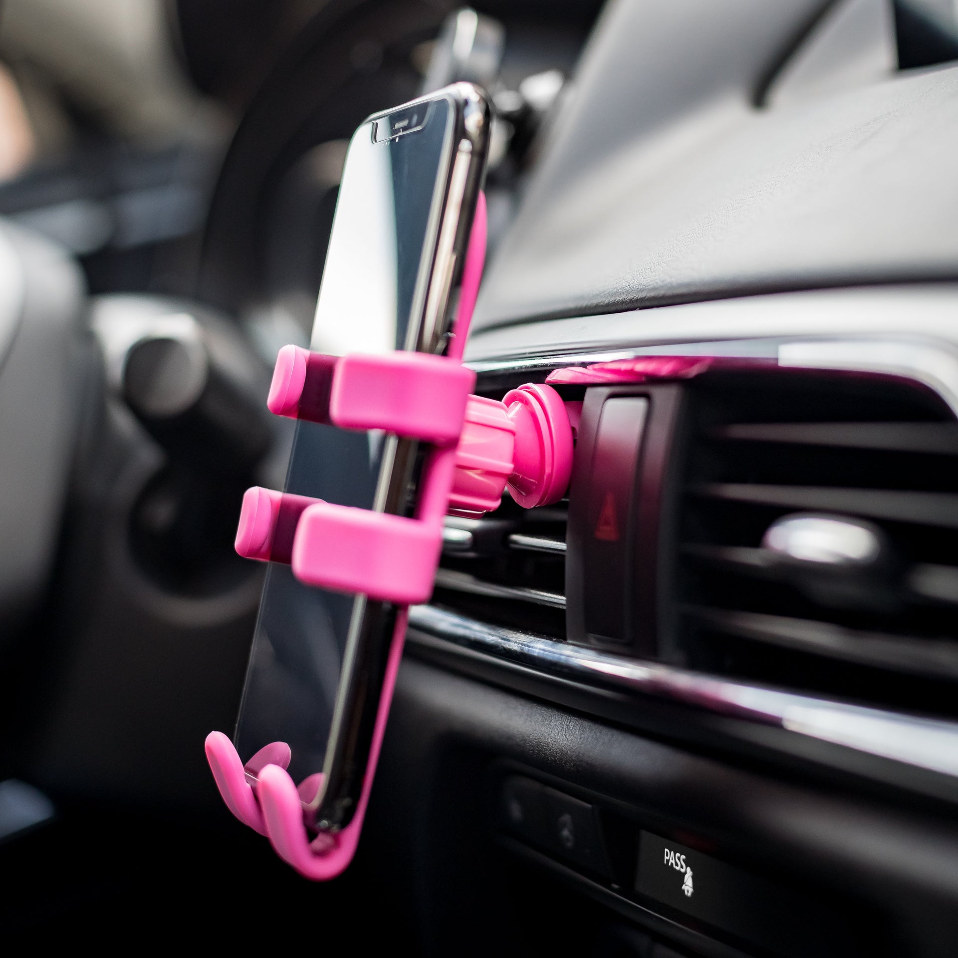 Image of OG Pink Hug Buddy holding a cell phone while attached to a vehicle air vent with a close up on the vent clip