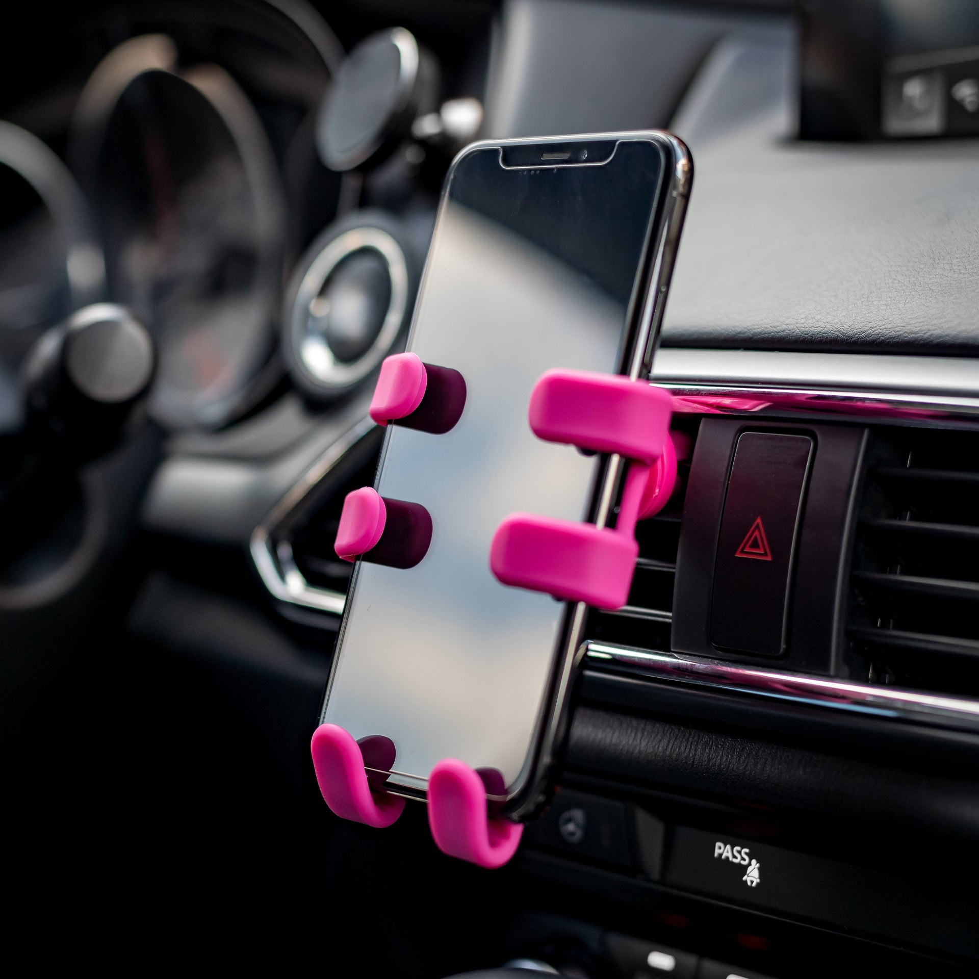 Image of OG Pink Hug Buddy holding a cell phone while attached to a vehicle air vent