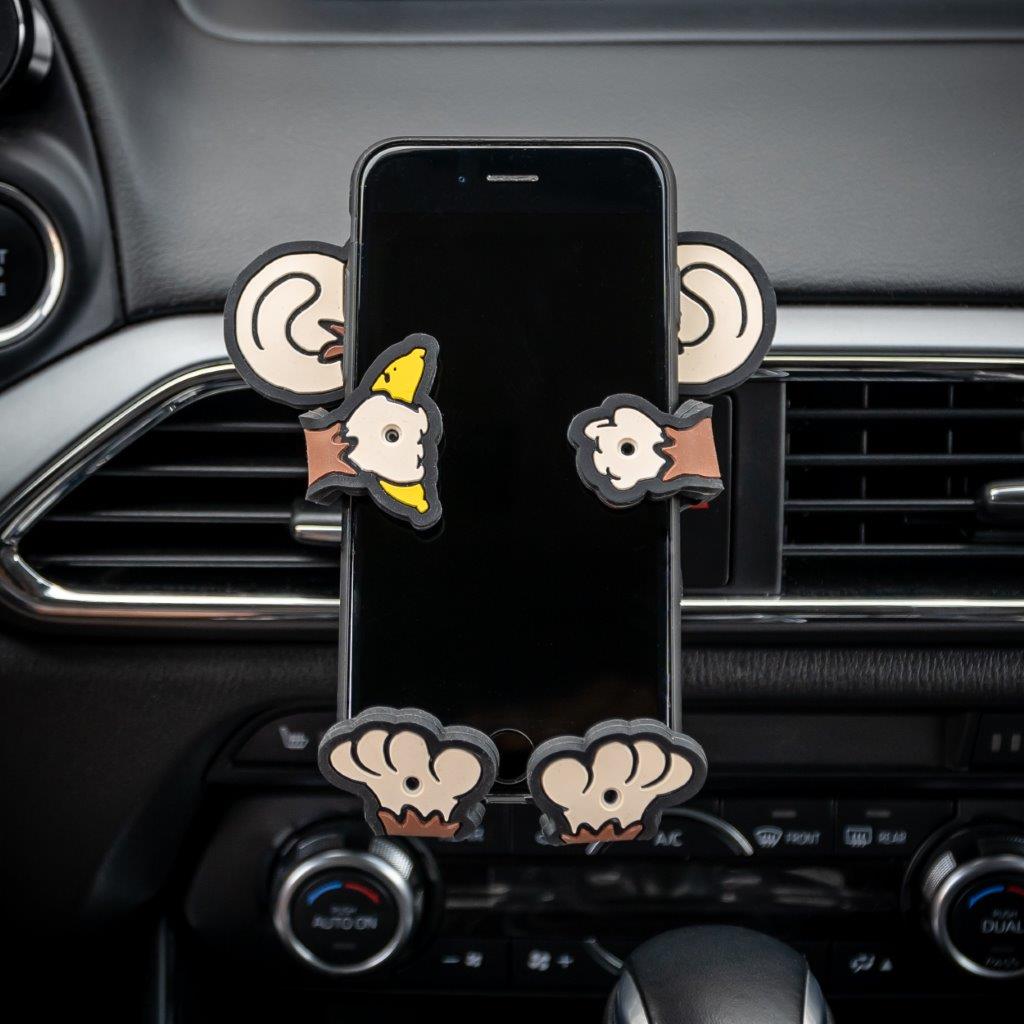 Image of Monkey Hug Buddy attached to a car air vent, holding a cell-phone.