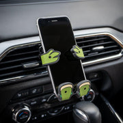 Image of Shellebrity the Turtle Hug Buddy attached to a car air vent with a cell-phone in its grasp