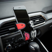 Image of Shaky the fish bait Hug Buddy holding a cell-phone in a vehicle, attached to its air vent