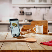 Image of Coolio the dog Hug Buddy holding a phone, resting on the vent clip on top of a kitchen island displaying a recipe on the screen, surrounded by cooking utensils