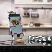 Image of OG Black Hug Buddy holding a cell-phone with a recipe displayed on screen, on top of a kitchen counter surrounded by kitchen utensils