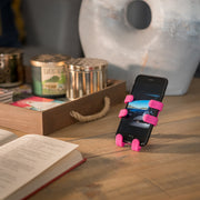 Image of OG Pink Hug Buddy holding a cell phone while sitting on a home office desk beside an open book