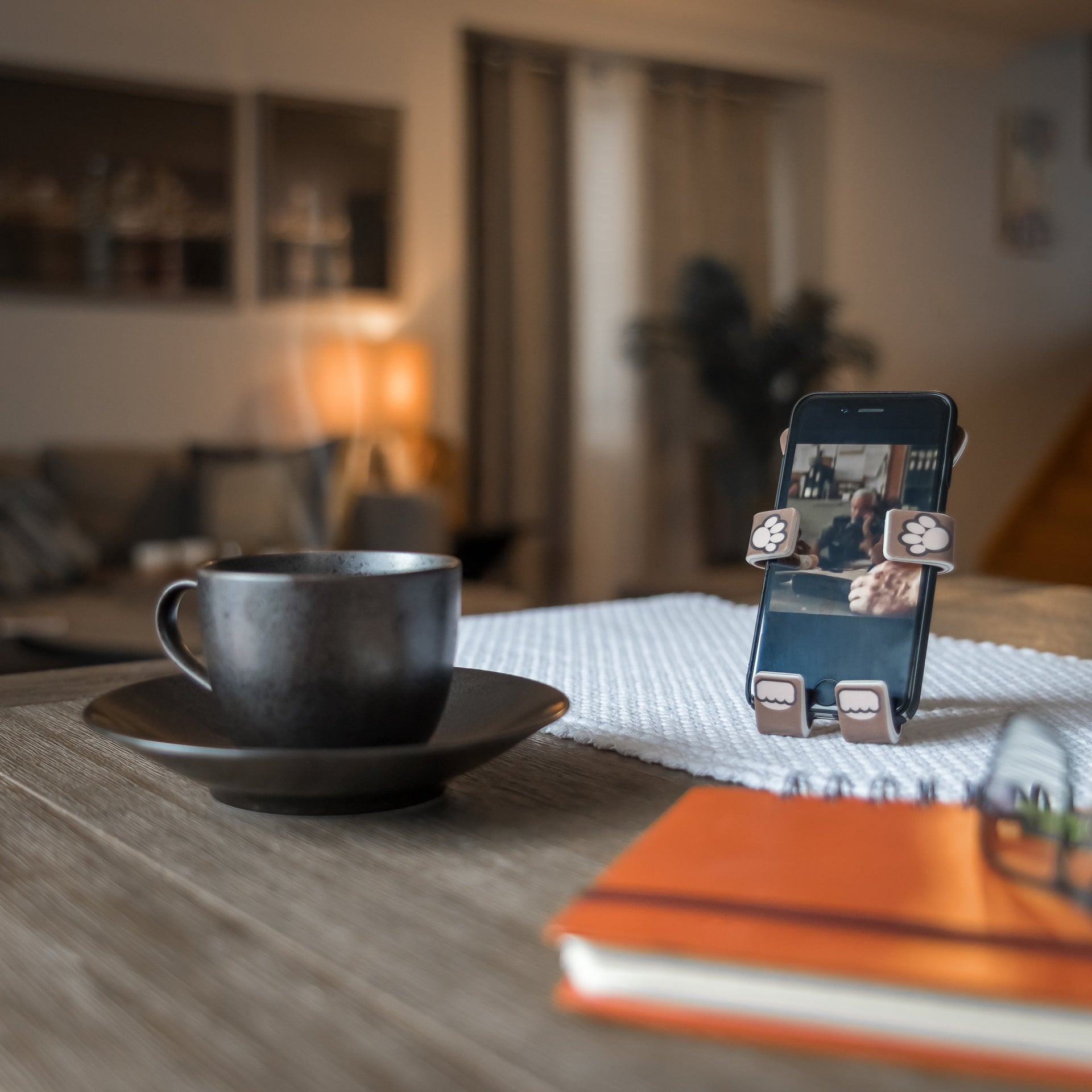 Image of Pug the dog Hug Buddy holding a cell phone while sitting on a kitchen table beside a hot cup of coffee