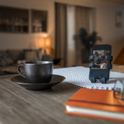 Image of OG Black Hug Buddy holding a cell phone while sitting on a kitchen table beside a hot cup of coffee