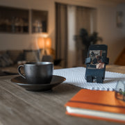 Image of Panda Hug Buddy sitting on a kitchen table, holding a phone, with a warm cup of coffee next to it.