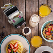 Image of OG Black Hug Buddy holding a cell-phone on top of a kitchen table surrounded by a breakfast feast